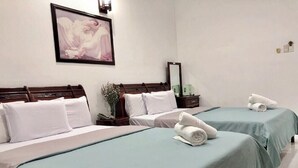 Une chambre d’hôtel avec deux lits, chacun recouvert d’une couverture verte, agrémenté d’oreillers blancs et de serviettes pliées posées sur les lits. Un tableau encadré orne le mur, et une table de chevet porte une lampe et une petite plante.