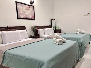 A hotel room with two beds, each with a green bedspread, white pillows, and rolled towels on the beds. There is a framed picture on the wall and a nightstand with a lamp and a small plant. - Mai Vy (Ho Chi Minh City)