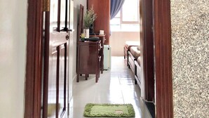Un couloir avec un cadre de porte en bois, un bureau avec un miroir, une petite plante et un lit avec un rideau bleu.