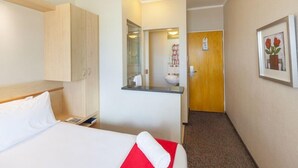 A hotel room with a bed, a wooden wardrobe, a bathroom with a sink and mirror, and a framed picture on the wall. - Road Lodge Gqeberha (Gqeberha)