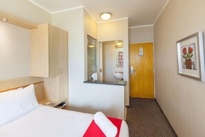 Habitación de hotel con cama, armario de madera, baño con lavamanos y espejo, y un cuadro en la pared.