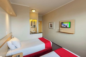 Habitación de hotel con dos camas, un televisor montado en la pared y un espejo sobre la cama.
