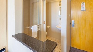 A bathroom with a granite countertop, a glass shower enclosure, a wooden door, and a visible toilet. - Road Lodge Gqeberha (Gqeberha)