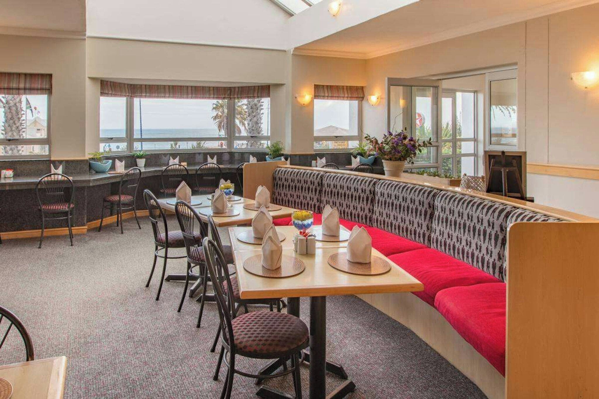 A restaurant with a high ceiling, large windows, and a seating area with a red cushioned bench.