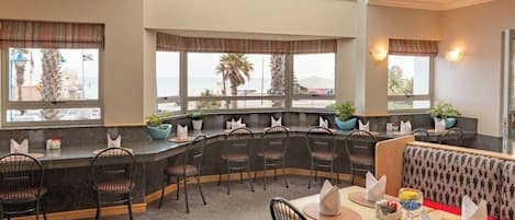 Ein Restaurant mit einer gebogenen Bar, einer Sitzgelegenheit und großen Fenstern mit Blick auf den Strand.