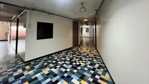 A hallway with a checkered floor pattern, a black square on the wall, and a ceiling light fixture. - Junction Hostels (Makati)