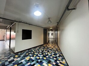 Un couloir avec un sol à motifs à carreaux, un carré noir sur le mur et un luminaire au plafond.