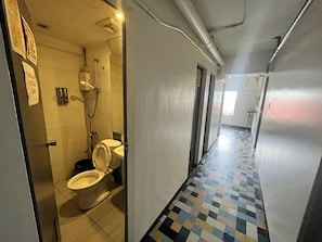 A narrow hallway with a tiled floor, a shower area, and a toilet. - Junction Hostels (Makati)