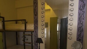 A dormitory room with bunk beds, a desk, a chair, a mirror, and a patterned curtain. - Junction Hostels (Makati)