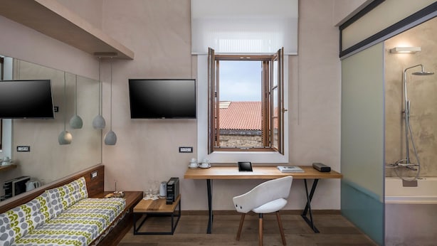 A compact room with a bed, a desk with a chair, a television, and a shower area.