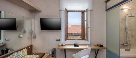 A compact room with a bed, a desk with a chair, a television, and a shower area.