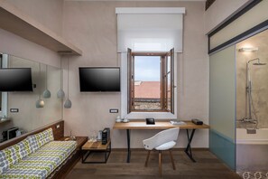 A compact room with a bed, a desk with a chair, a television, and a shower area. - Ambassadors Residence (Chania)