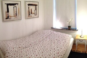 Un dormitorio con una colcha estampada con motivos florales, una mesita de noche con lámpara y dos cuadros abstractos enmarcados en la pared.