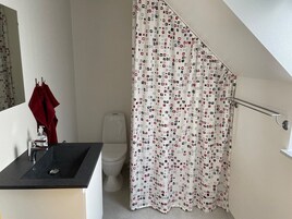 Un baño con un lavamanos negro, una toalla roja, un inodoro y una cortina de ducha con diseño geométrico.