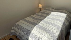A single bed with a striped bedspread, a bedside lamp, and two abstract paintings on the wall. - Herning City Apartments (Herning)
