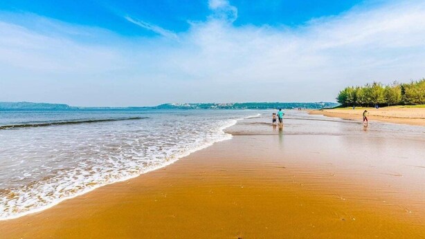 A beach with a clear sky, calm sea, and a few people walking. - At Home B&B Dona Paula (Panaji)