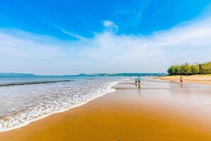 Una playa con cielo despejado, mar tranquilo y algunas personas caminando.