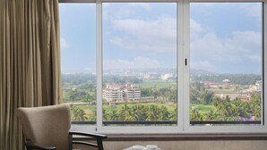 A room with a large window offering a view of a cityscape and greenery. - At Home B&B Dona Paula (Panaji)