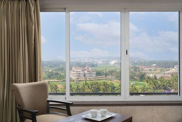 A room with a large window offering a view of a cityscape and greenery. - At Home B&B Dona Paula (Panaji)