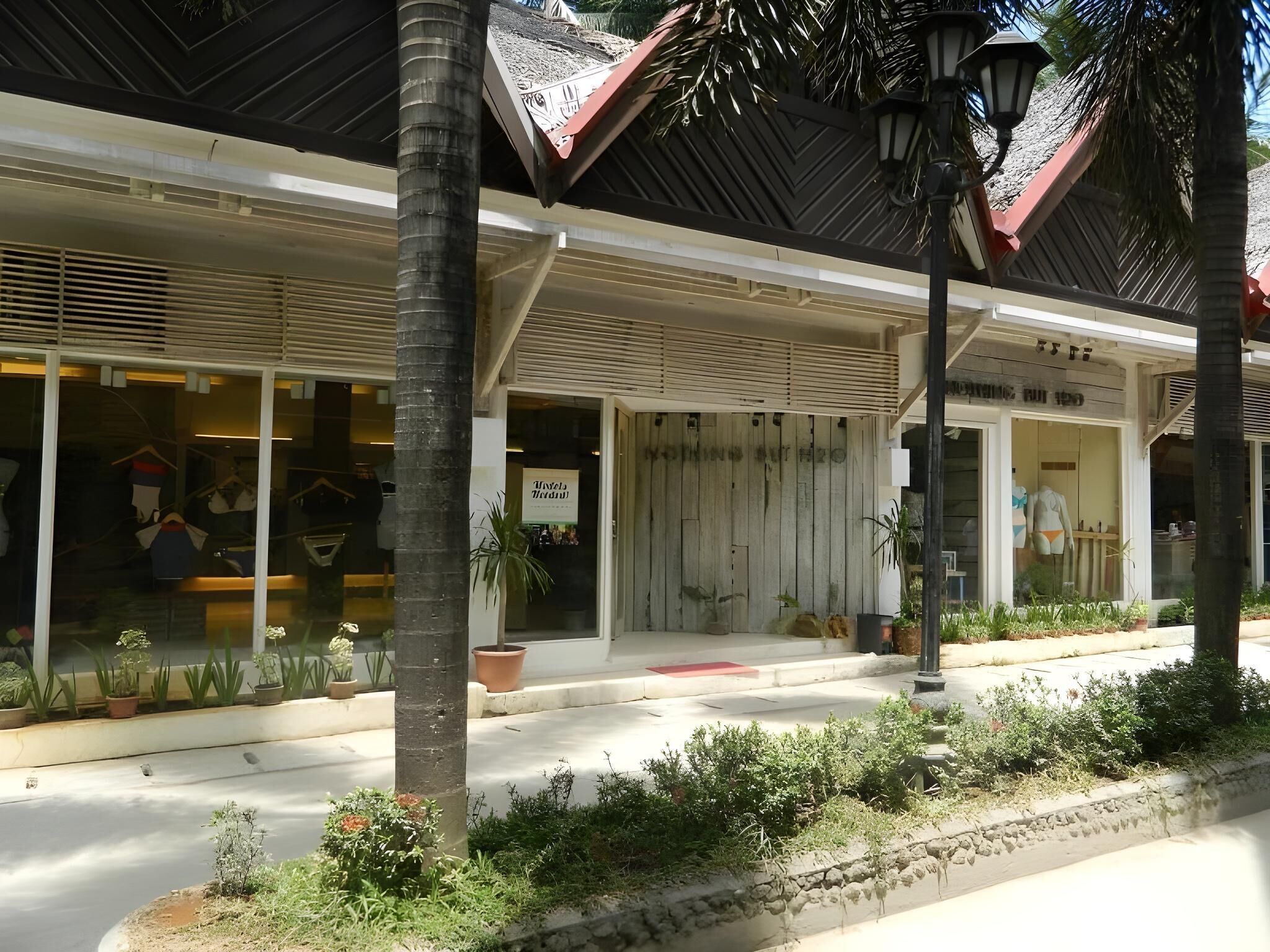 A building with a modern architectural style, featuring a flat roof and large windows. There are potted plants and a street lamp in front of the building.
