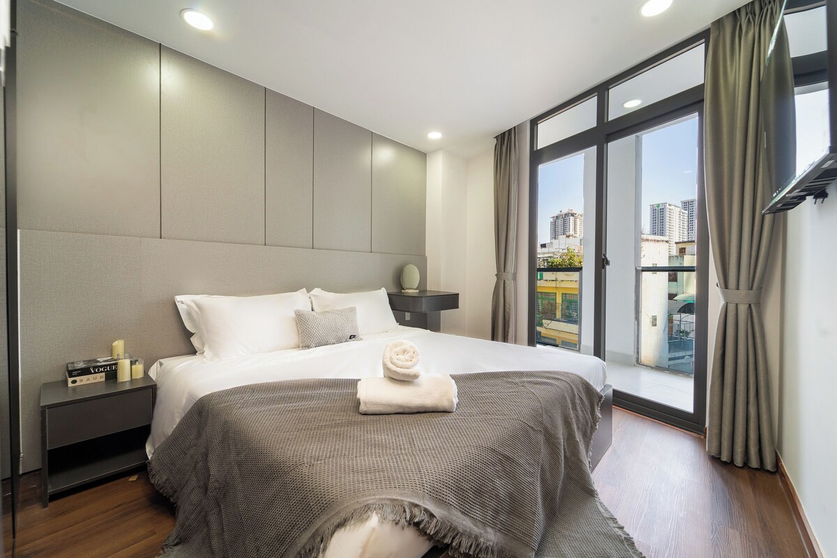 Ein modernes Hotelzimmer mit einem großen Bett, einem Nachttisch, einem Fenster mit Vorhängen und Blick auf die Stadt.