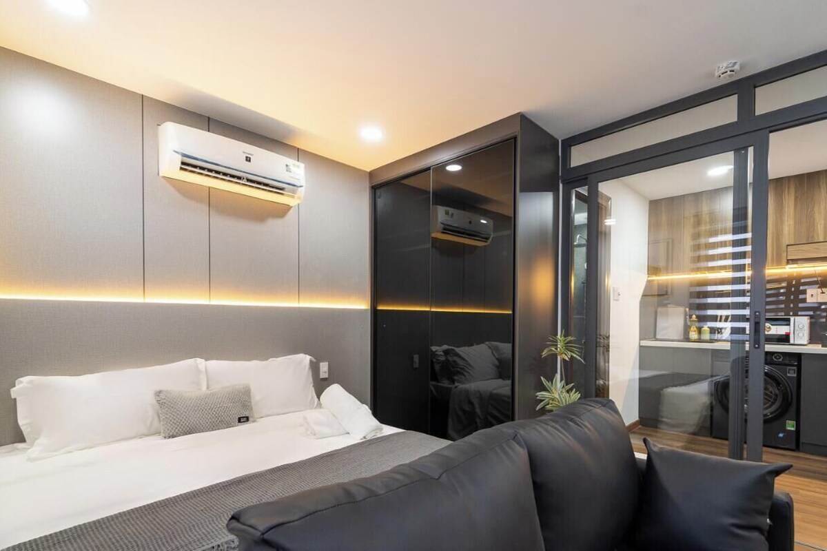 Ein modernes Hotelzimmer mit einem Bett, einem Sofa, einer Klimaanlage und einer Glastür, die zu einer Küchenzeile führt.