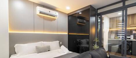 Une chambre d’hôtel moderne équipée d’un lit, d’un canapé, d’un appareil de climatisation et d’une porte-fenêtre coulissante donnant sur un coin cuisine.