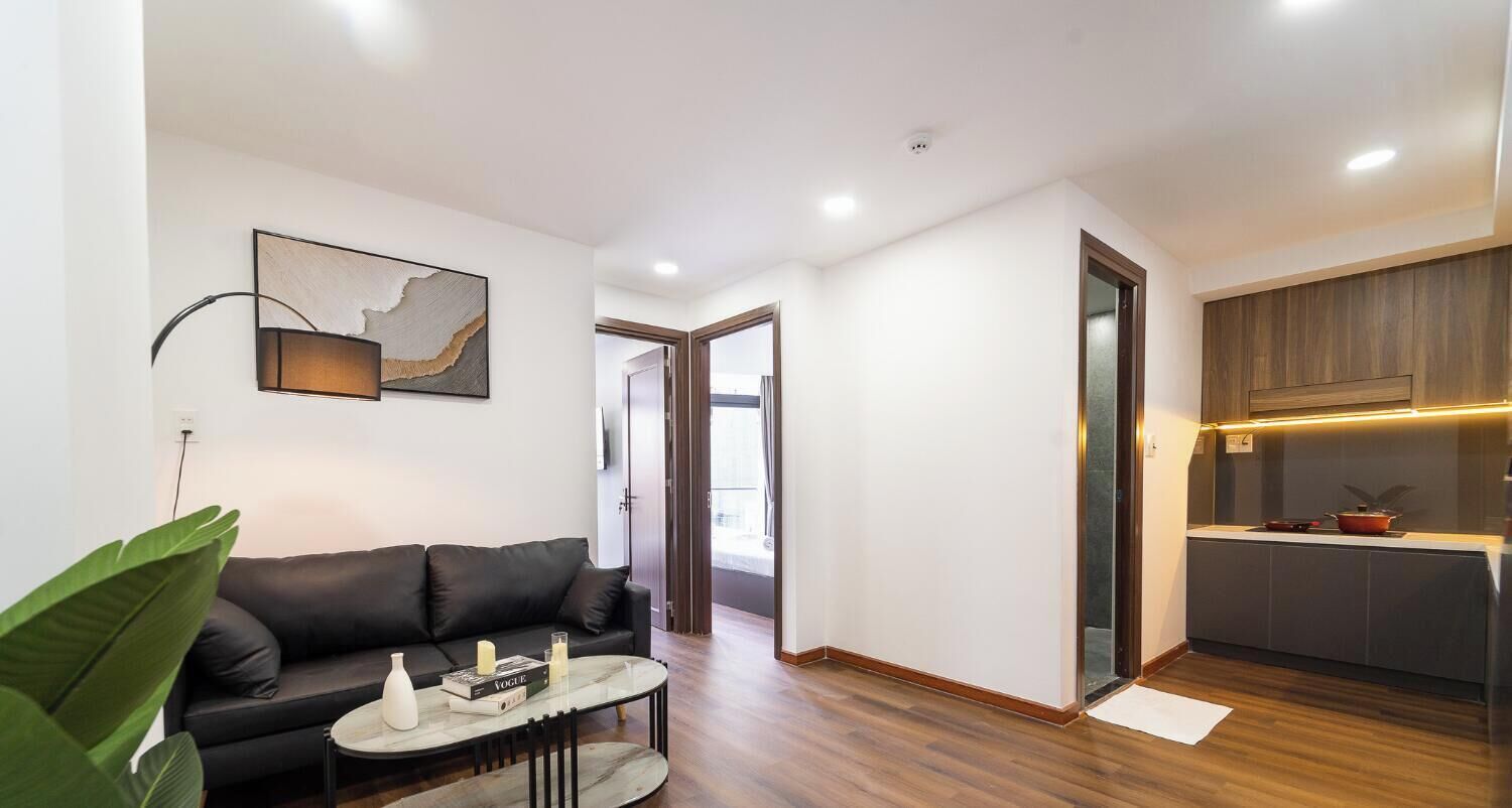 A modern living room with a black leather sofa, a round coffee table, and a large plant.