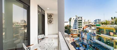 Un balcón con mesa y sillas, equipos de aire acondicionado y vista a la ciudad.