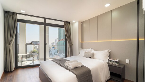 Une chambre d’hôtel moderne dotée d’un grand lit, d’une table de chevet et offrant une vue sur la ville grâce à de grandes fenêtres du sol au plafond.