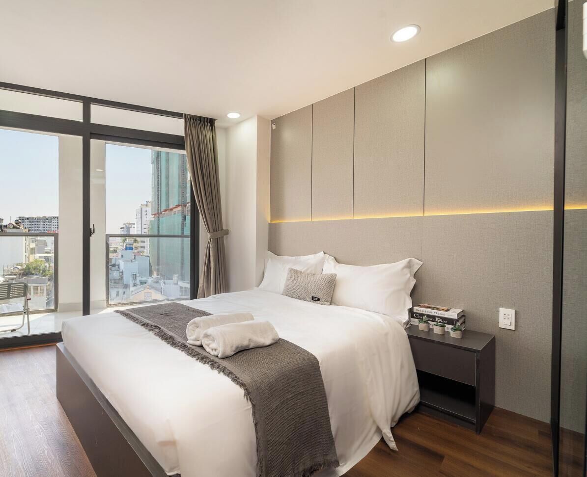 A modern hotel room with a large bed, a nightstand, a view of the city, and a cityscape visible through the window.