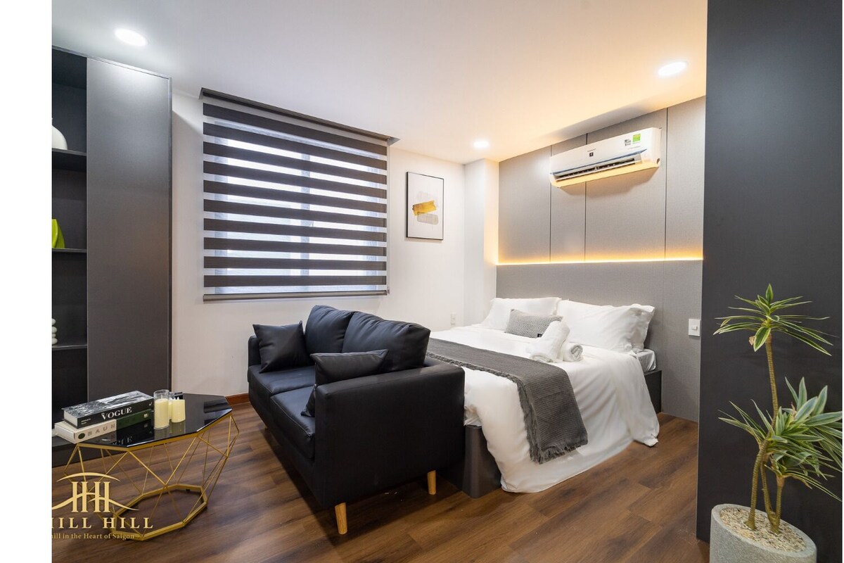 Ein modernes Hotelzimmer mit einem Bett, einer Couch, einem kleinen Tisch mit Büchern und einer Topfpflanze.
