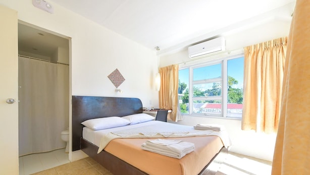 Ein Hotelzimmer mit Bett, Nachttisch, Klimaanlage und einem Vorhangfenster.