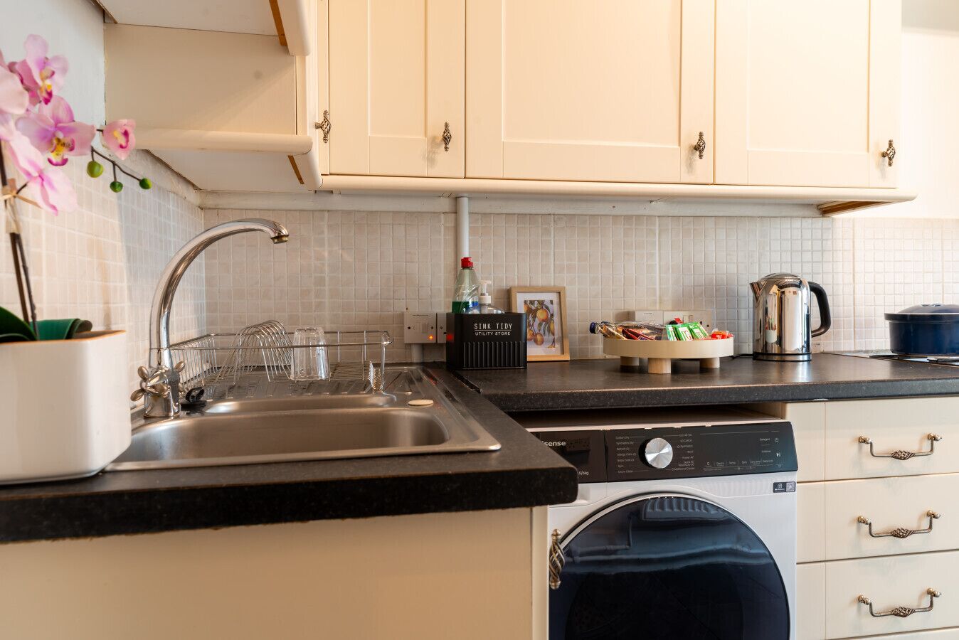 A kitchen with a sink, dishwasher, and cabinets. There is a plant, a kettle, and a bottle on the counter.