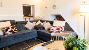Ein modernes Wohnzimmer mit einer Eckcouch, einem kleinen Tisch, einer Fernbedienung und einer Pflanze.