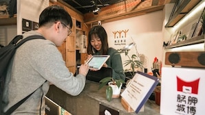A reception desk with a wooden interior, a sign with the text "Meeting Mates", and a person holding a tablet. - Duckstay Hostel (Taipei)
