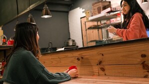 A person sitting at a wooden counter in a cafe, holding a red cup. - Duckstay Hostel (Taipei)