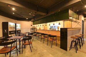 A modern bar area with wooden tables and chairs, a counter with stools, and a refrigerator with beverages. - Duckstay Hostel (Taipei)