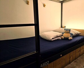 A bunk bed with a blue mattress and a wooden headboard. There are pillows and a stuffed toy on the bed. - Duckstay Hostel (Taipei)