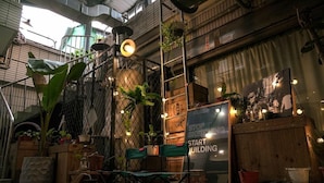 An outdoor seating area with chairs and tables, surrounded by plants and a wooden fence. - Duckstay Hostel (Taipei)