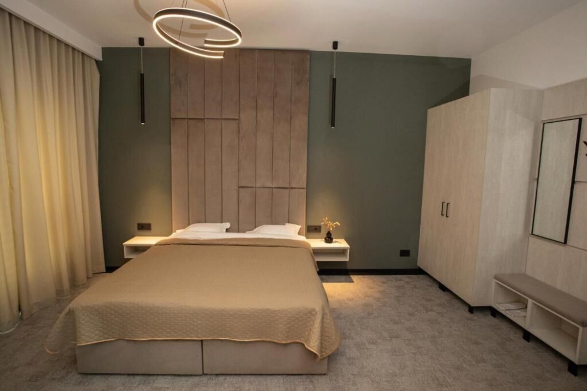A modern bedroom with a large bed, a wooden headboard, a bedside table with a lamp, and a wardrobe.