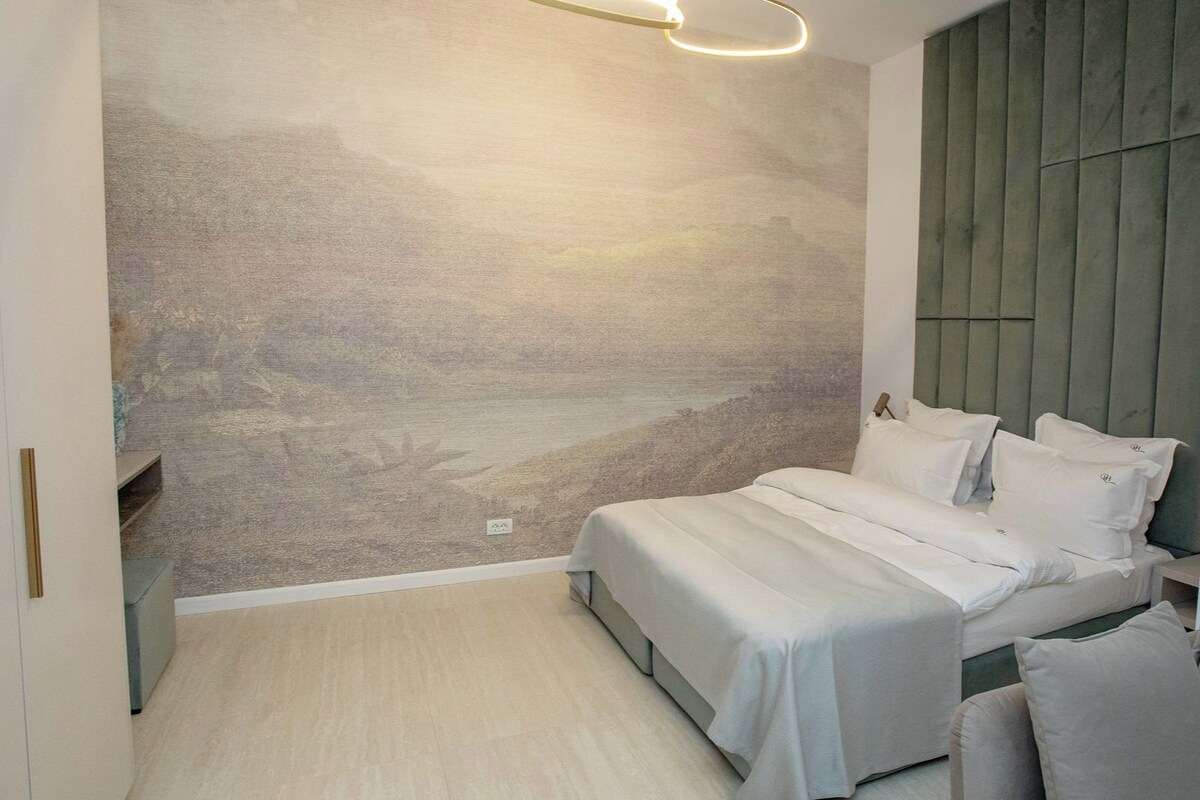 A bedroom with a bed, bedside tables, a wall-mounted headboard, and a hanging light fixture.