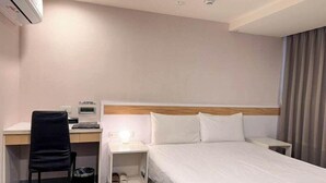 A hotel room with a bed, a desk, a chair, a nightstand, and an air conditioning unit. - 9ine Hotel (Taipei)