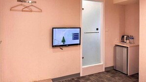A hotel room with a television mounted on the wall, a door with frosted glass, and a small kitchenette area with a refrigerator and a coffee maker. - 9ine Hotel (Taipei)