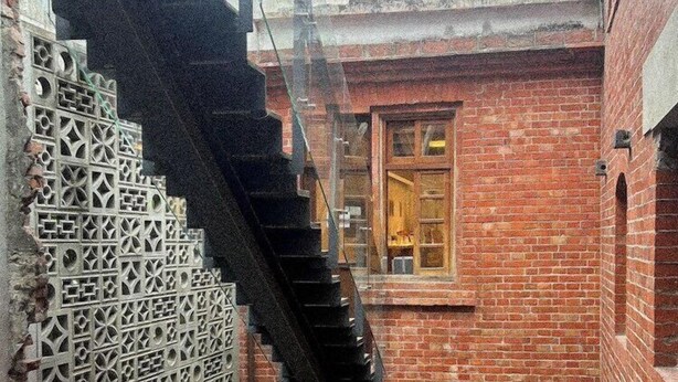 A narrow alleyway with a brick building, a glass staircase, and a metal fence. - 9ine Hotel (Taipei)