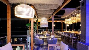 An outdoor dining area with round tables and chairs, a wooden ceiling, and hanging lights. - Art Hotel (Kassandra)