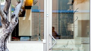 A hotel entrance with a glass door, a metal handle, and a reflection of a person inside. - Art Hotel (Kassandra)