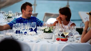 A couple seated at a table with multiple wine glasses, a white tablecloth, and a view of the sea. - Art Hotel (Kassandra)