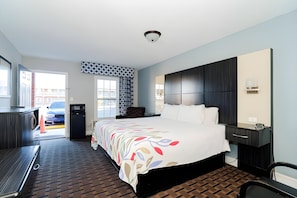 A hotel room with a large bed, a desk, a chair, a wardrobe, and a view of the outside. - Emerson Inn (Jacksonville)