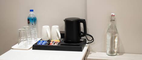 Un angolo cottura con una macchina da caffè, una bottiglia d'acqua, una bottiglia di vetro e un vassoio con tazze e snack.